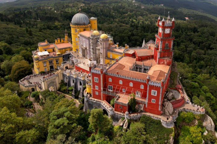 Colorful castle with red and yellow towers surrounded by forested hills.
