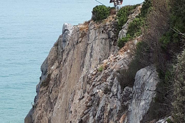 Person fishing on a steep rocky cliff next to the ocean.