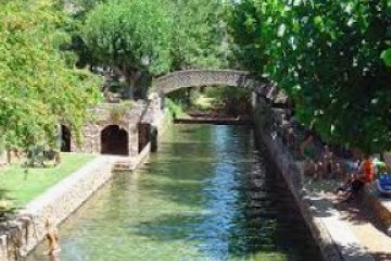 Stone bridge over a narrow canal surrounded by greenery and trees.