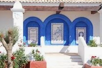 Outdoor wall with three blue arches and decorative tiles, surrounded by plants.