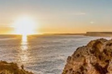 Sunset over the ocean with rocky cliffs in the foreground.