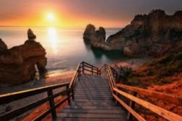 Wooden stairs lead to a beach with rocky cliffs at sunset.