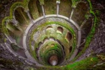 Spiral stone staircase with arches, covered in moss, viewed from above.