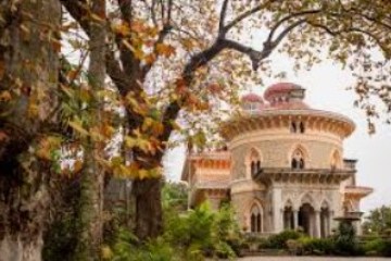 Historic building with domes and arches beside trees with autumn leaves.
