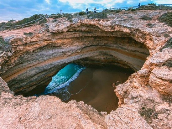Natural rocky cave with an opening to a beach and ocean waves inside.