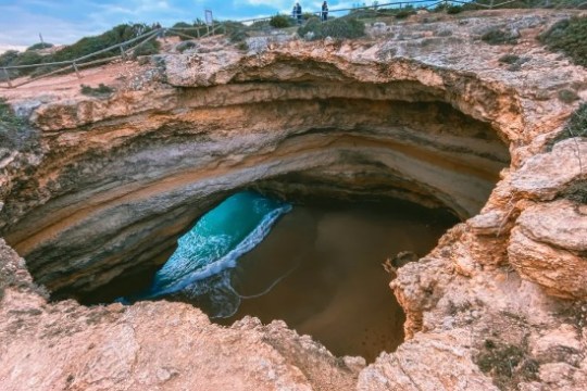 Natural rocky cave with an opening to a beach and ocean waves inside.