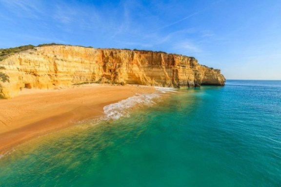 Golden cliffs and sandy beach with turquoise sea under a blue sky.