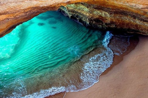 Beach cave with turquoise water and wavy sand patterns.