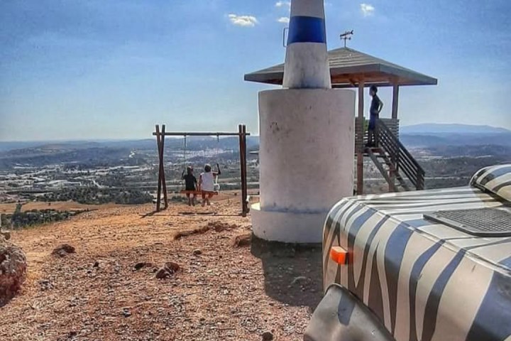 People on swings by a lookout tower, zebra-patterned vehicle in foreground, landscape views in the background.