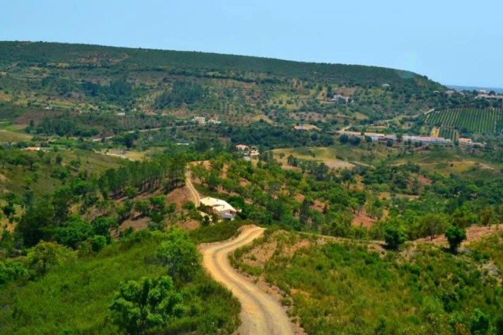 Winding dirt road through hilly green landscape under a clear blue sky.