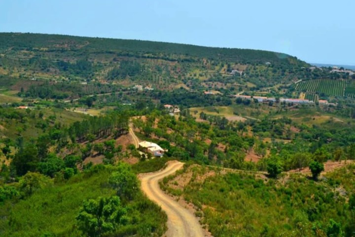 Rural landscape with winding dirt road, hills, and scattered houses.