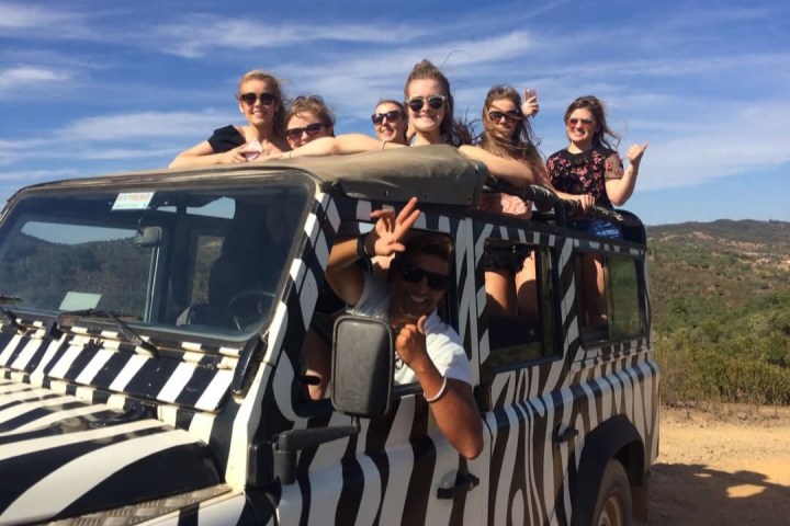 Group of people in a zebra-striped safari vehicle on a sunny day.