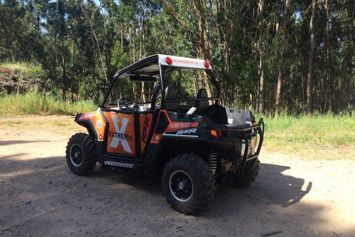 Black and orange off-road vehicle parked on a dirt path near tall trees.