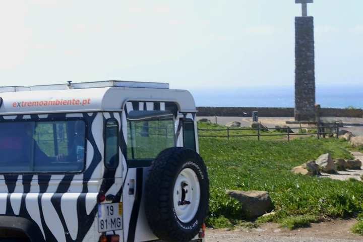 Zebra-striped vehicle parked near a grassy area with a stone cross monument in the background.