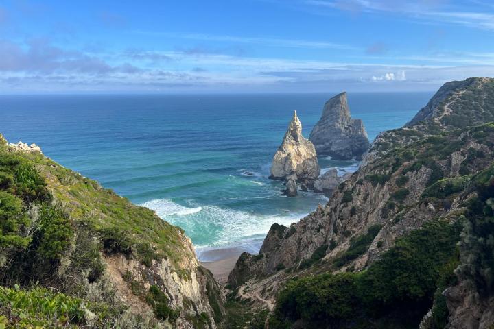 Rocky cliffs and sea stacks with waves in a coastal landscape under a blue sky.