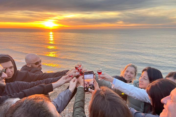 Group of people toasting near a sunset over the ocean.