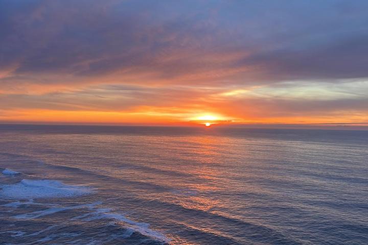 Sunset over the ocean with colorful clouds and gentle waves.