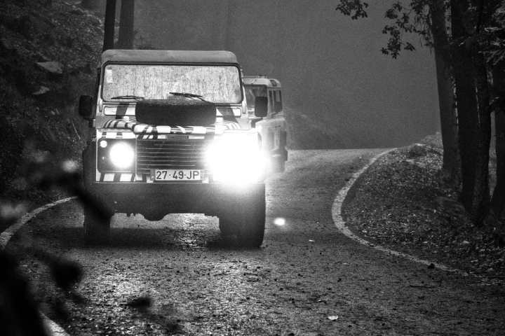 Two off-road vehicles drive along a foggy forest road in a black and white photo.
