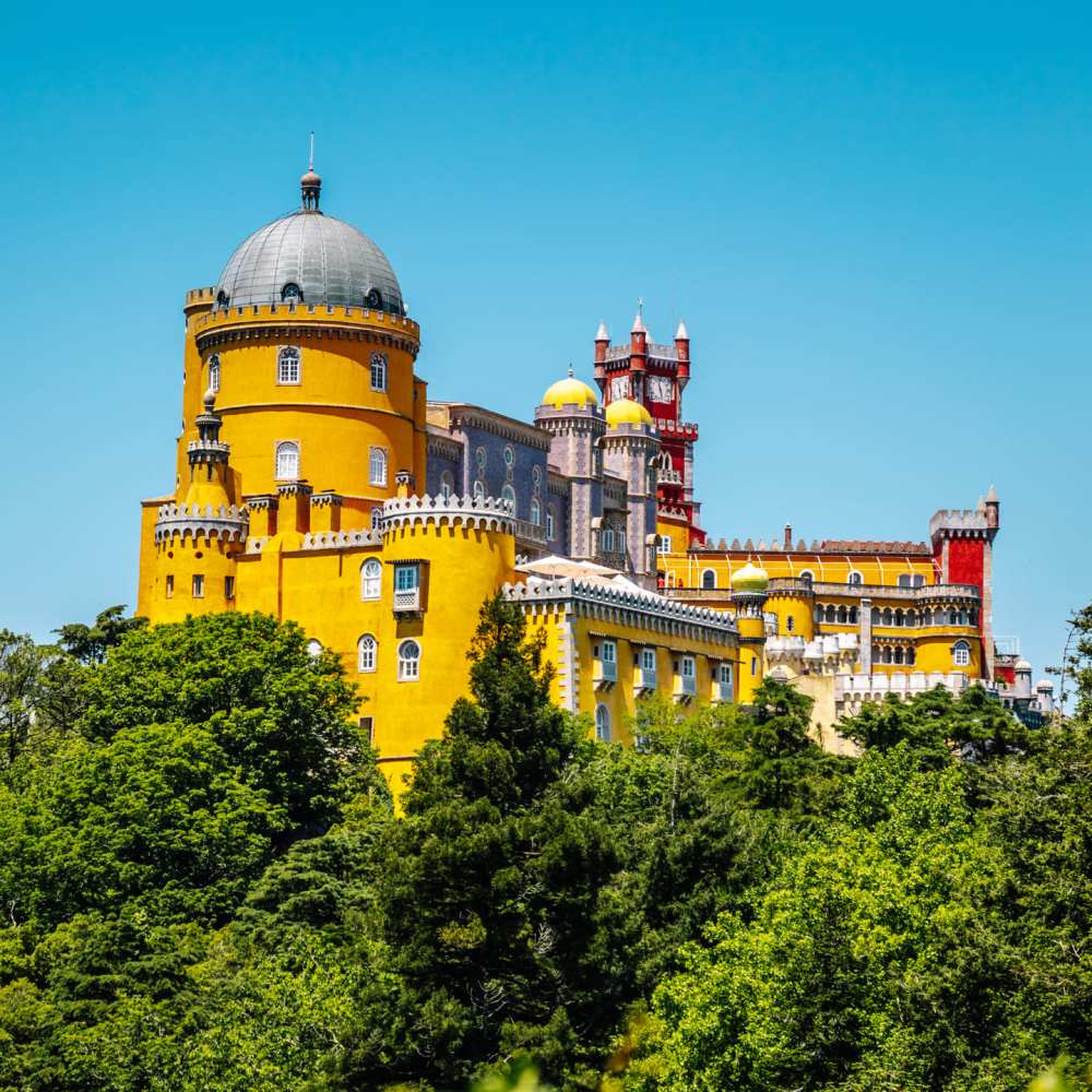 Colorful castle with yellow and red walls surrounded by greenery under a clear blue sky.