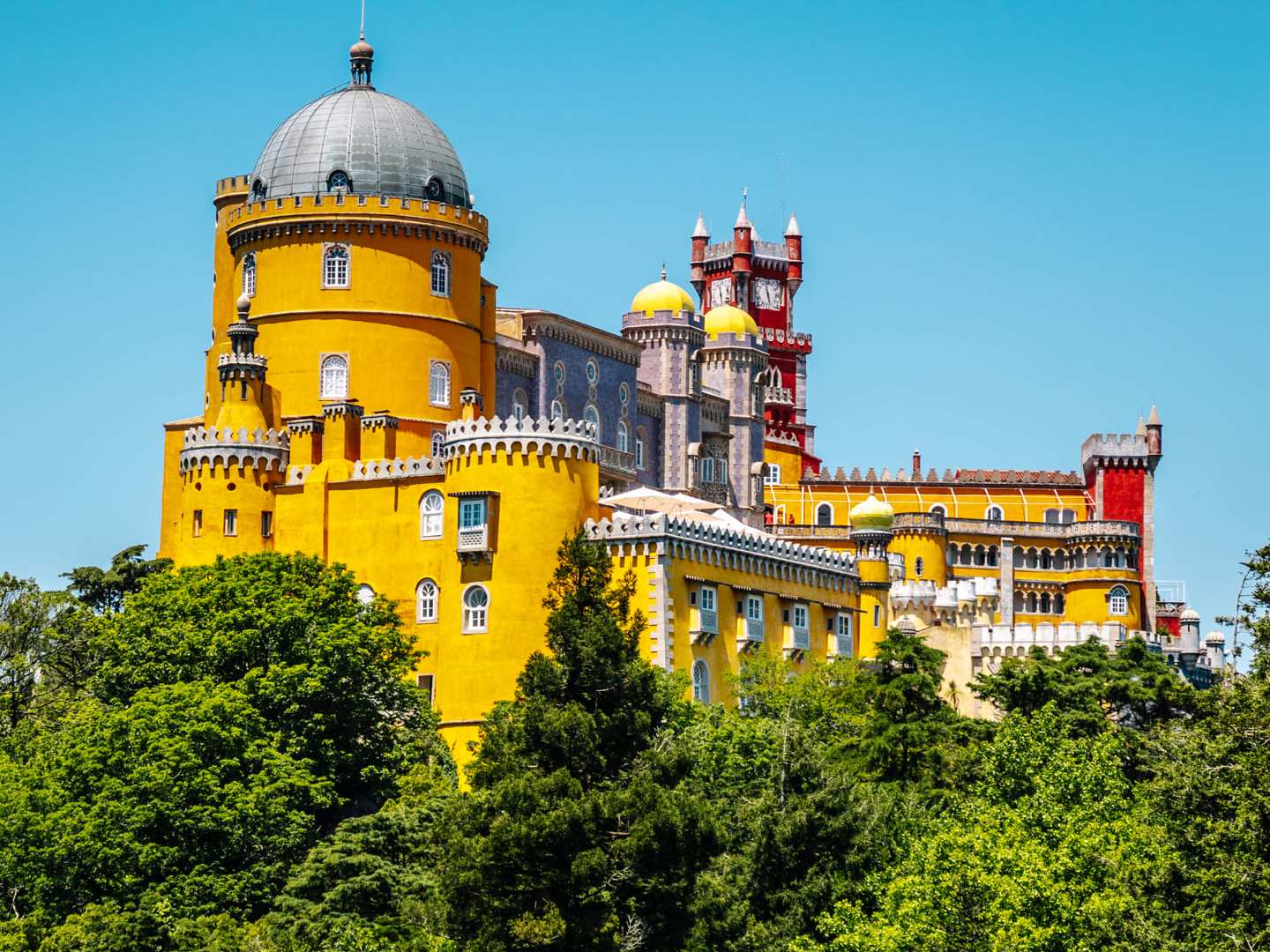 Colorful castle with yellow and red walls surrounded by greenery under a clear blue sky.