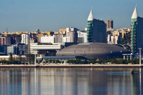 Waterfront cityscape with domed building and twin spire structures under clear blue sky.