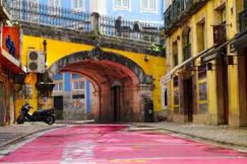 Colorful alley with pink pavement, yellow buildings, archway, and parked scooter.