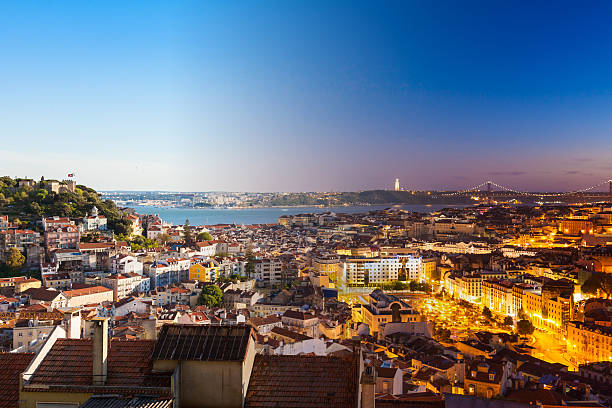 Cityscape of Lisbon at dusk with illuminated buildings and Tagus River.