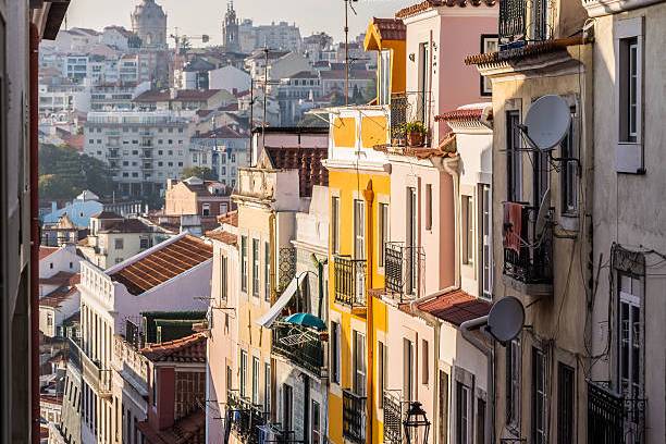 Colorful buildings on a steep street overlook a cityscape with distant towers.