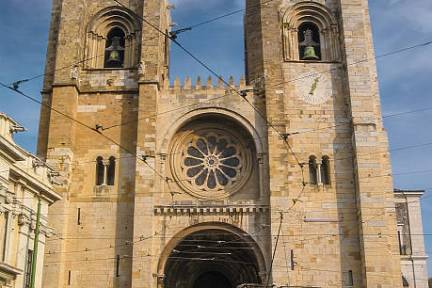 Historic tram passing by Se Cathedral in Lisbon under a clear sky.