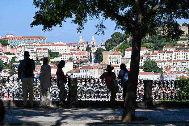 Silhouetted people under trees overlooking a hilly cityscape with colorful buildings.