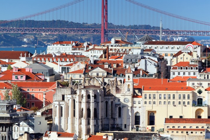 Panoramic view of a city with red rooftops and a large red suspension bridge in the background.