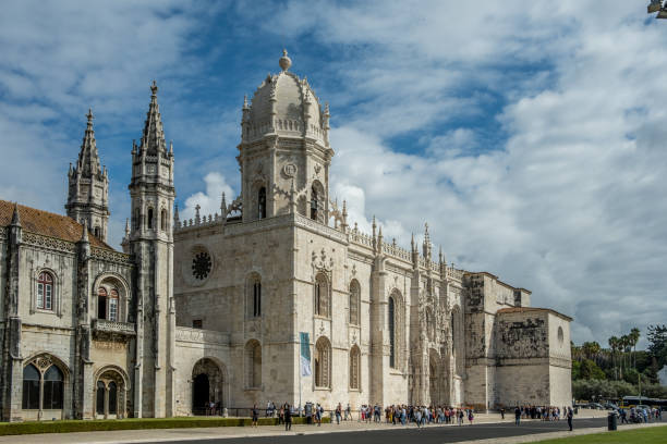 Gothic-style historic building with ornate towers and tourists outside on a cloudy day.