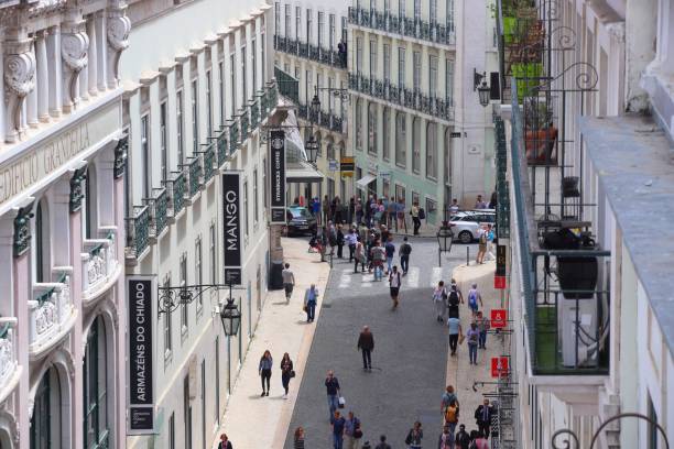 People walking on a narrow street flanked by buildings with store signs in a city.
