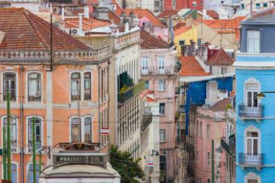 Yellow tram on a narrow street with colorful buildings in Lisbon.