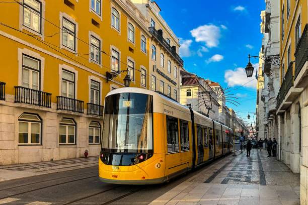 Yellow tram on city street with historic buildings and blue sky background.