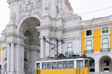 Yellow tram in front of a historic stone archway and building with statues.