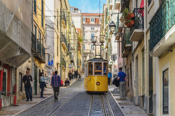 Yellow tram on a narrow, cobblestone street with people walking in a European city.