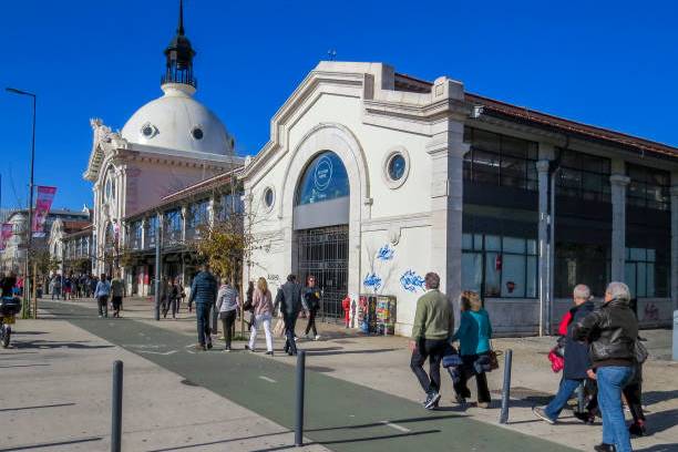 People walk by a historic building with a dome under a clear blue sky.