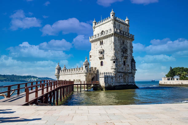 Historic stone tower by the sea with a wooden walkway under a blue sky.