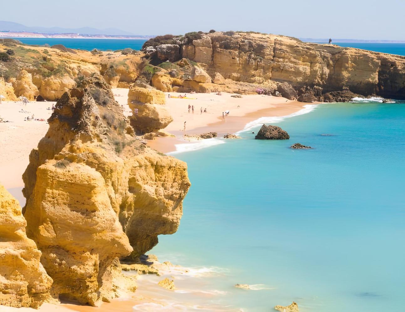 Scenic beach with rocky cliffs and turquoise water on a sunny day.
