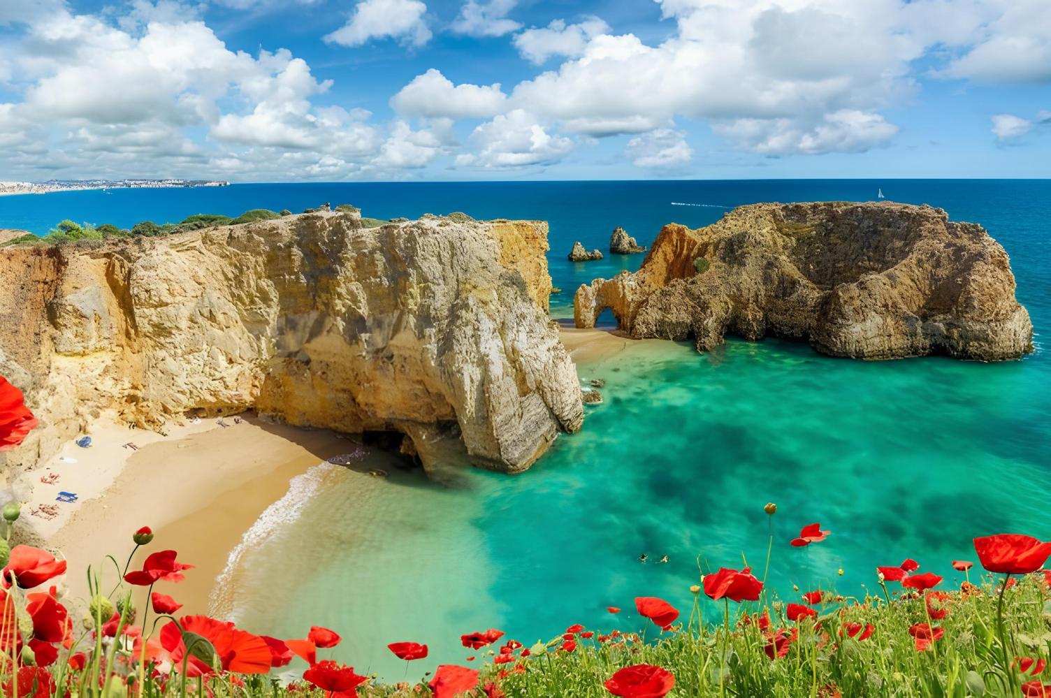 Coastal cliffs, turquoise sea, sandy beach, red poppies in foreground, and scattered clouds in blue sky.