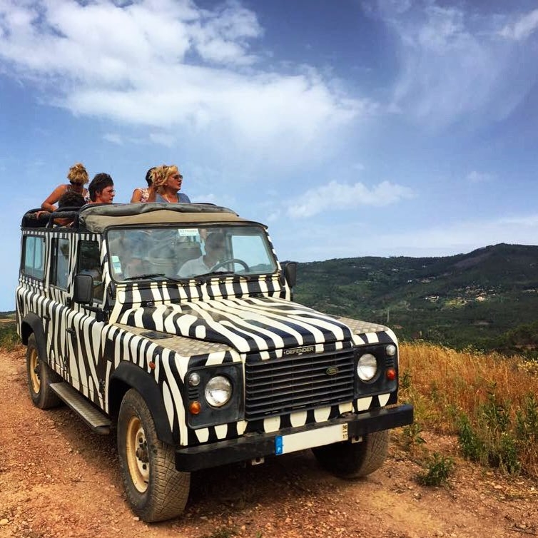 Zebra-striped vehicle on a dirt road with people inside and scenic hilly background.