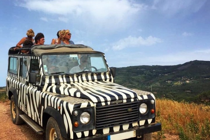 Zebra-striped vehicle on a dirt road with people inside and scenic hilly background.
