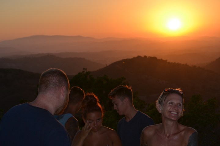 Group of people smiling at sunset in hilly landscape.