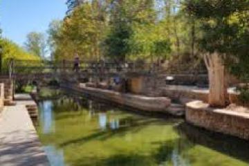 Scenic view of a canal with a stone bridge and trees.