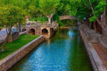 Serene canal with stone bridges and lush greenery on both sides.