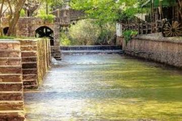Narrow river with steps on the sides, stone bridge, and trees overhead.