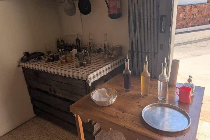 Small rustic bar with bottles on tables, checkered cloth, and a tray.