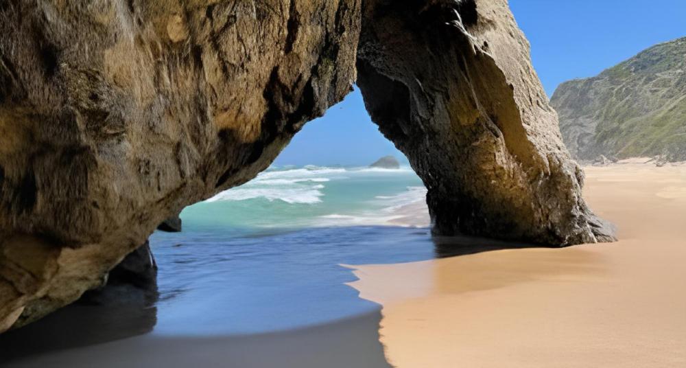 Rocky archway on sunny beach, ocean waves visible.